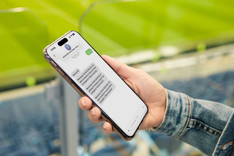 Mano sosteniendo un teléfono inteligente en un estadio deportivo enviando mensajes de texto a IOLAN SCRC para habilitar una conexión celular