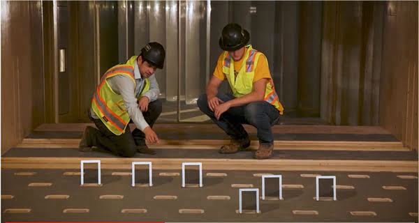 Two technicians wearing safety gear discuss six 'roughness' blocks protruding from the wind tunnel floor.